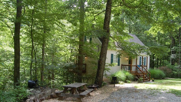 A rustic cabin surrounded by dense forest, with a gravel path leading to a wooden picnic table and a small outdoor seating area. - Couples Mountain Retreat (Montebello)