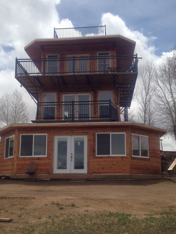 A multi-story wooden cabin with a balcony on the upper floor, large windows, and a door with a glass panel.