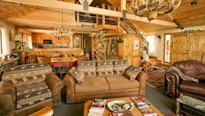 A rustic interior with a wooden ceiling, a sofa with patterned cushions, a leather armchair, and a chandelier. - Private Lodge-Mtn Lake, Pool,Hot Tub, Affordable Family Reunion Sleeps 20+ (Westcliffe)
