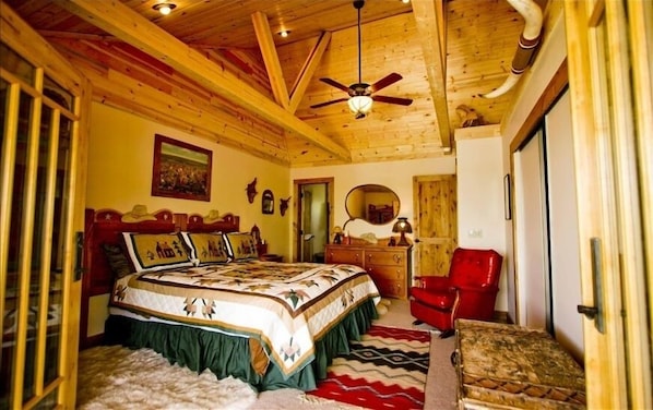 A bedroom with a wooden ceiling, a bed with a patterned bedspread, a red chair, and a wooden dresser.