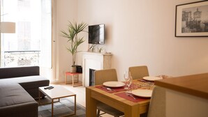 A dining area with a table set for two, a sofa, a TV, and a fireplace. - Family-friendly apartment in an authentic neighborhood and its open market (Nice)