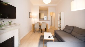 A modern living room with a flat-screen TV, a fireplace, a sofa, a dining area with chairs, and a kitchen in the background. - Family-friendly apartment in an authentic neighborhood and its open market (Nice)
