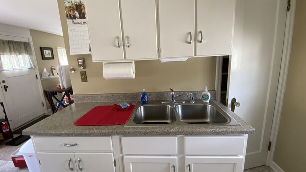 A kitchen with white cabinets, a granite countertop, a red cutting board, a sink, and a calendar on the wall. - Perfect for two! Less than half mile from Yellowstone. 'Downtown' location. (Gardiner)