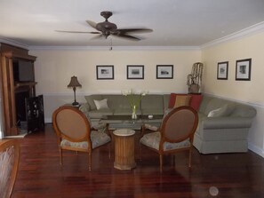 A living room with a ceiling fan, a sofa, two armchairs, a coffee table, and framed pictures on the wall.