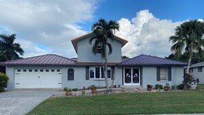 A two-story house with a garage, a front porch, and a well-maintained lawn. - Quiet Culdesac, Golf Course view, 3 Bedroom 2 Bath, Sleeps 8! (Marco Island)