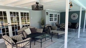 A covered patio area with a sectional sofa, armchairs, a glass coffee table, and a dining table with chairs. - Quiet Culdesac, Golf Course view, 3 Bedroom 2 Bath, Sleeps 8! (Marco Island)