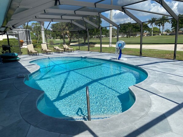 A swimming pool with a sunshade structure, surrounded by a patio area with lounge chairs and a view of a golf course. - Quiet Culdesac, Golf Course view, 3 Bedroom 2 Bath, Sleeps 8! (Marco Island)