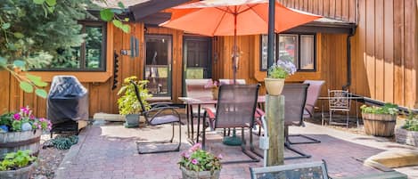 A wooden cabin with a patio area featuring outdoor furniture, a barbecue grill, and potted plants.