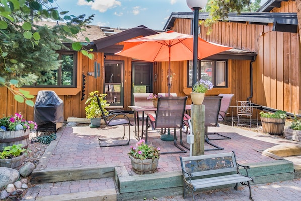 A wooden cabin with a patio area featuring outdoor furniture, a barbecue grill, and potted plants.