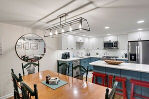 A modern kitchen with white cabinets, a stainless steel refrigerator, and a wooden dining table with chairs.