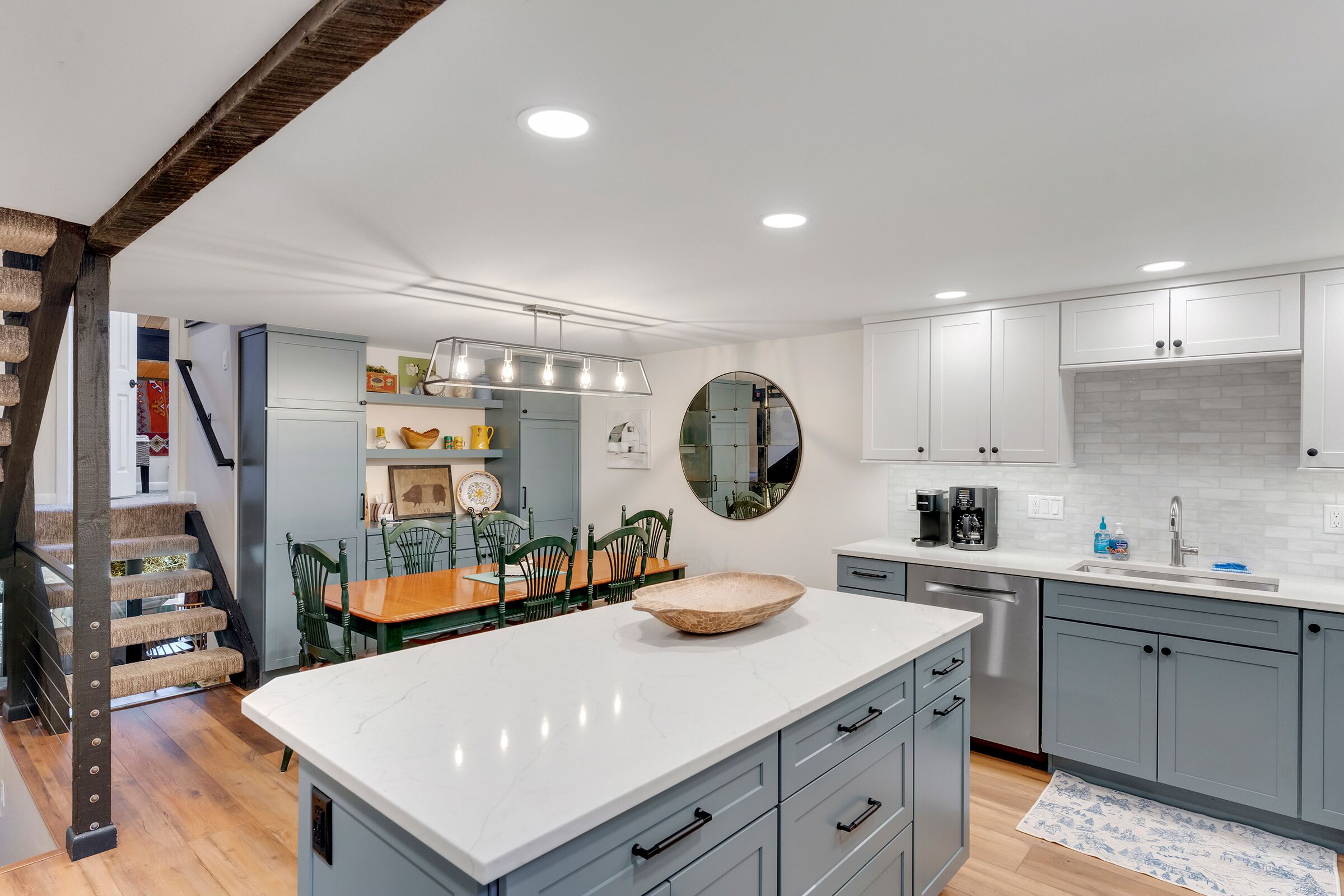 A modern kitchen with grey cabinets, a white countertop, and a wooden bowl centerpiece.