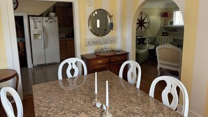A dining area with a granite table, white chairs, a ceiling fan, a kitchen in the background, and a sign that reads "SUMMER COTTAGE". - 
VENETIAN'27SEND INQUIRY! Walk to Everything/Fenced Yard/Enclosed Front Porch/AC (Charlevoix)