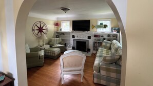 A cozy living room with a fireplace, striped armchairs, a checkered sofa, and a mounted fish decoration. - 
VENETIAN'27SEND INQUIRY! Walk to Everything/Fenced Yard/Enclosed Front Porch/AC (Charlevoix)