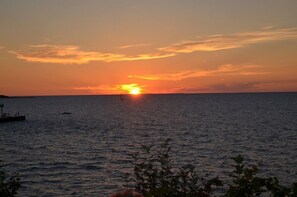 Ein Sonnenuntergang über einem ruhigen Meer mit einem Steg und einem Boot in der Ferne.