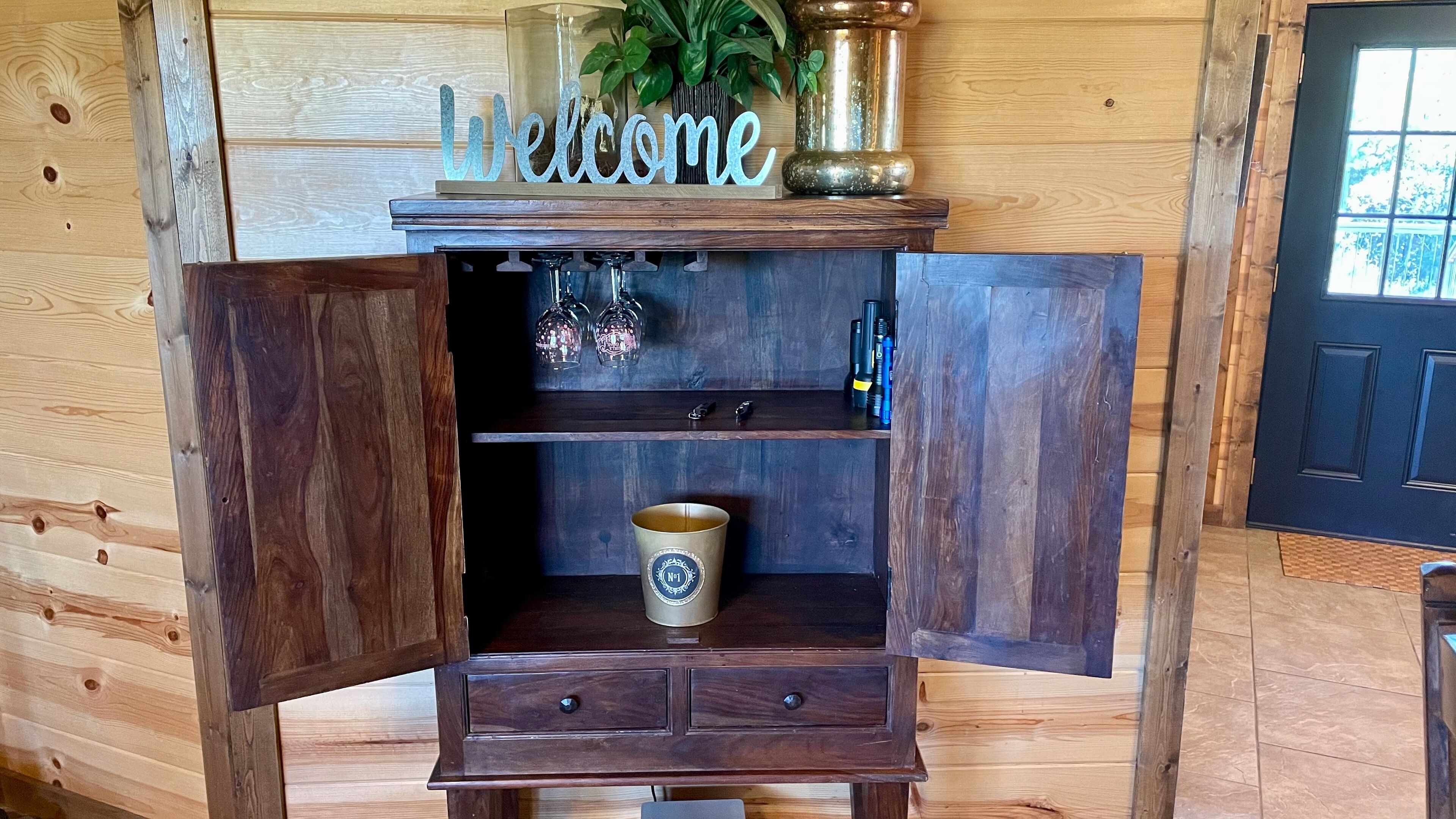 Un gabinete de madera con un cartel de 'Welcome', una lámpara decorativa y un letrero de 'No Fumar'.