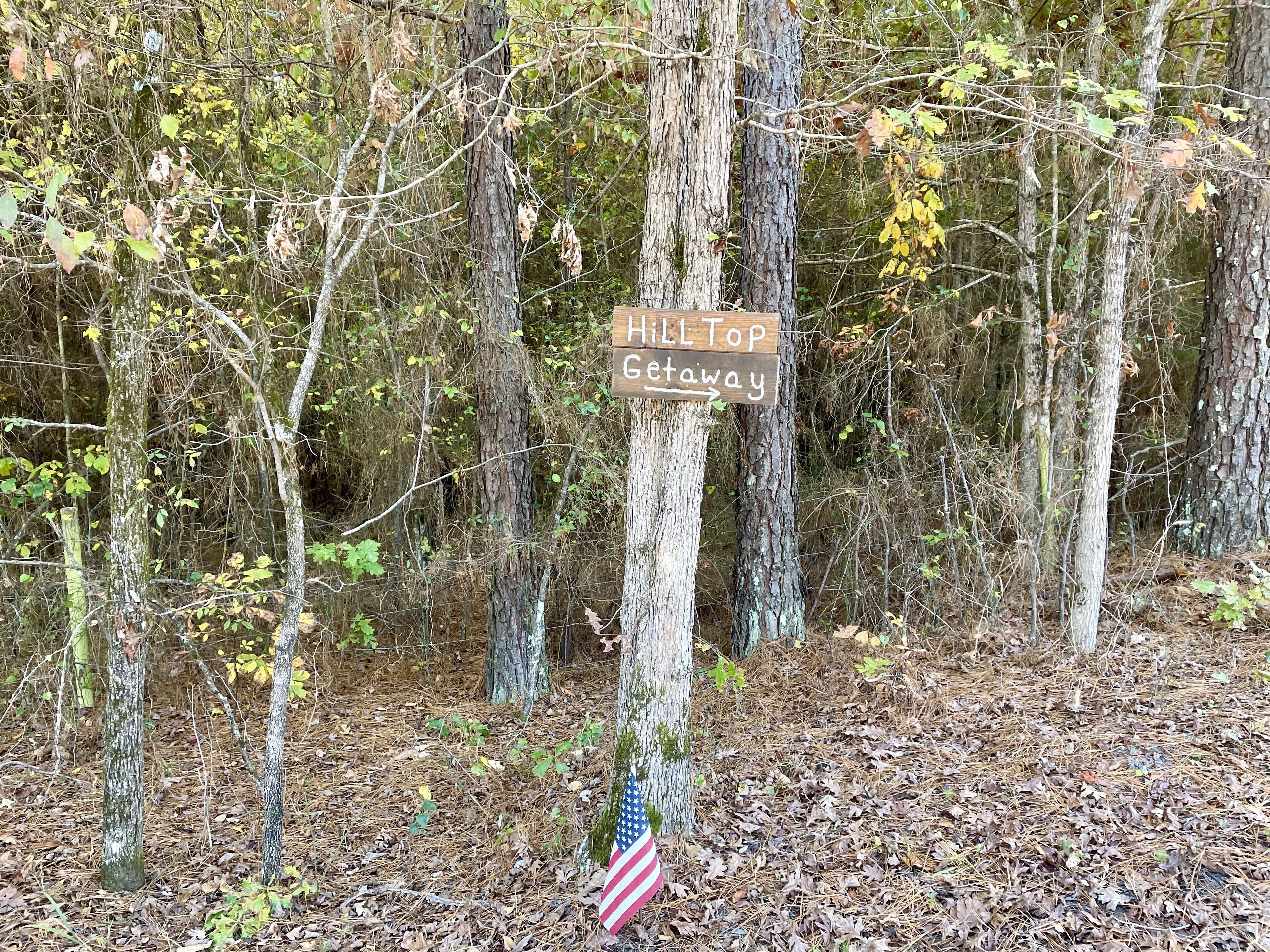 Ein Holzschild in bewaldeter Landschaft, am Fuße eine amerikanische Flagge.