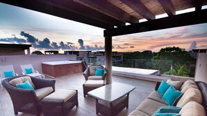 Una terraza en la azotea con mobiliario de mimbre, una mesa y vistas al atardecer.