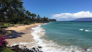 A beach with clear turquoise water, a sandy shore, and a backdrop of a mountain. - Amazing panoramic ocean view!   Perfect for couples. Just steps to the ocean.🏝 (Lahaina)