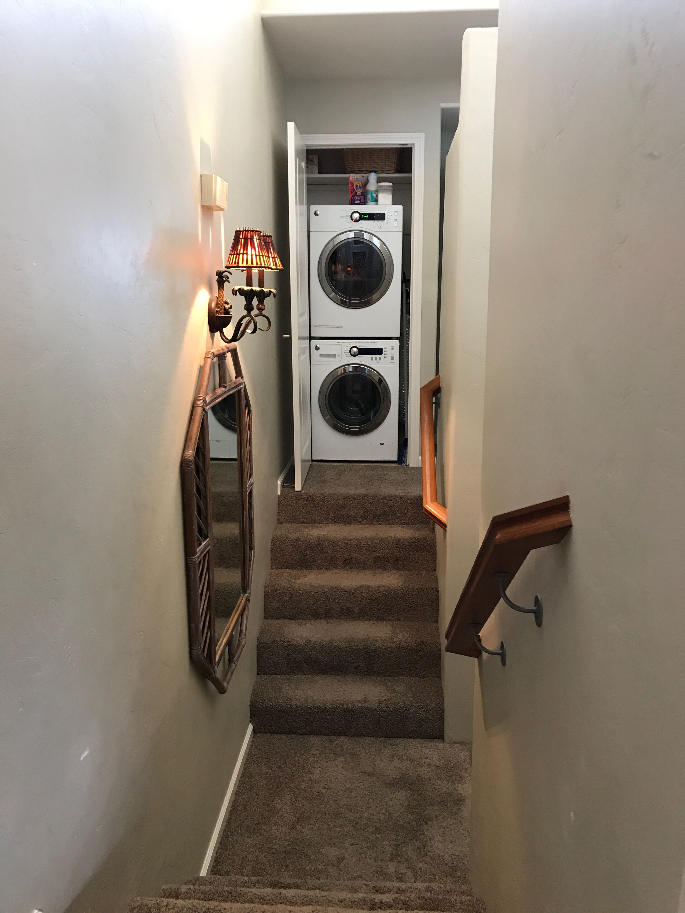 A narrow hallway with carpeted stairs leading to a laundry room containing two stacked washing machines.