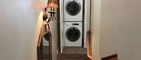 A narrow hallway with carpeted stairs leading to a laundry room containing two stacked washing machines.