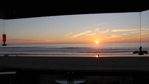 Vista a la playa desde un espacio techado con una mesa y sillas.