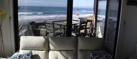 A room with a view of the ocean, a cushioned seating area with patterned pillows, and a table with chairs.