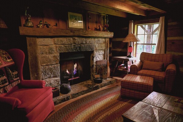 A cozy room with a stone fireplace, a red armchair, a plaid sofa, and a lamp on a wooden table.
