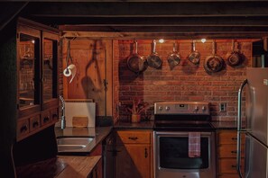 A kitchen with a brick wall, wooden cabinets, a stainless steel refrigerator, and hanging pots.