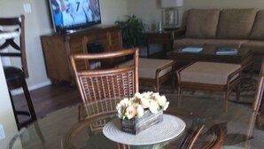 Un coin repas avec une table à plateau en verre, entourée de chaises en osier dotées d’assises rembourrées.