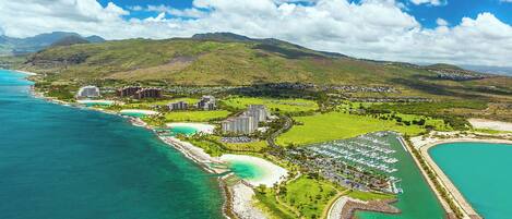 An aerial view of Koolina, Hawaii, featuring a coastal resort area with beachfront properties, a marina, and lush green hills in the background.