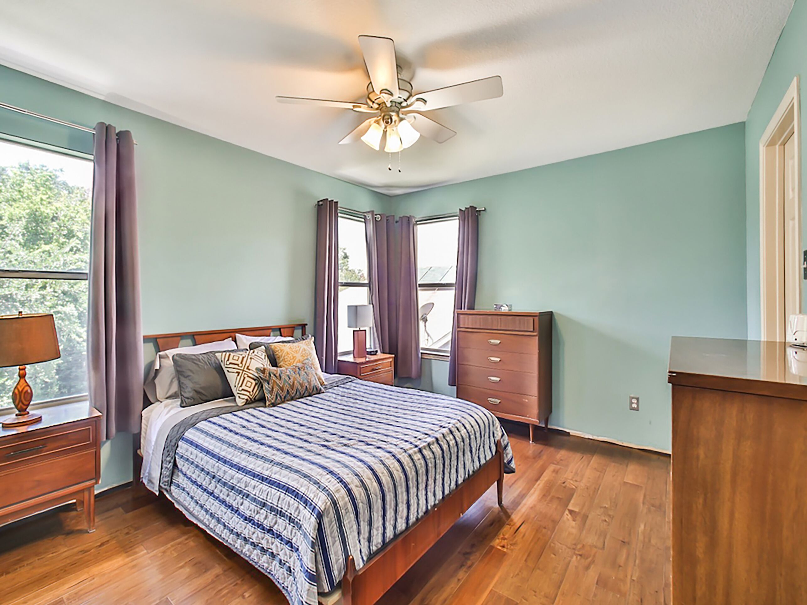 A bedroom with a bed, wooden dresser, nightstand, and a ceiling fan.