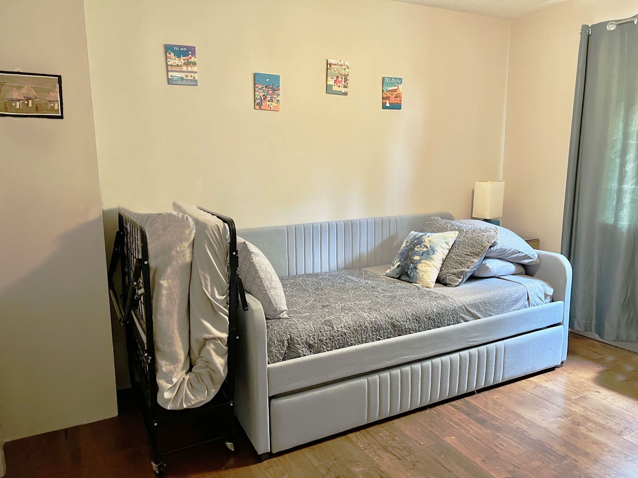 A small, light-colored sofa with a patterned cover, a single pillow, and a blanket draped over it. There are four small posters on the wall above the sofa.