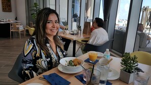 Un coin repas avec une table mise pour le repas, comprenant une assiette de nourriture, un verre de jus d’orange et une bouteille d’eau.
