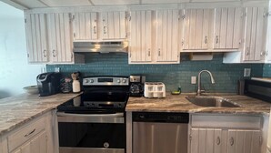Una cocina con electrodomésticos de acero inoxidable, armarios de madera clara y un salpicadero azul verdoso.