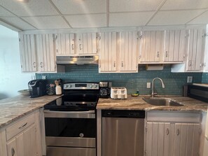 A kitchen with stainless steel appliances, light wood cabinets, and a teal backsplash.