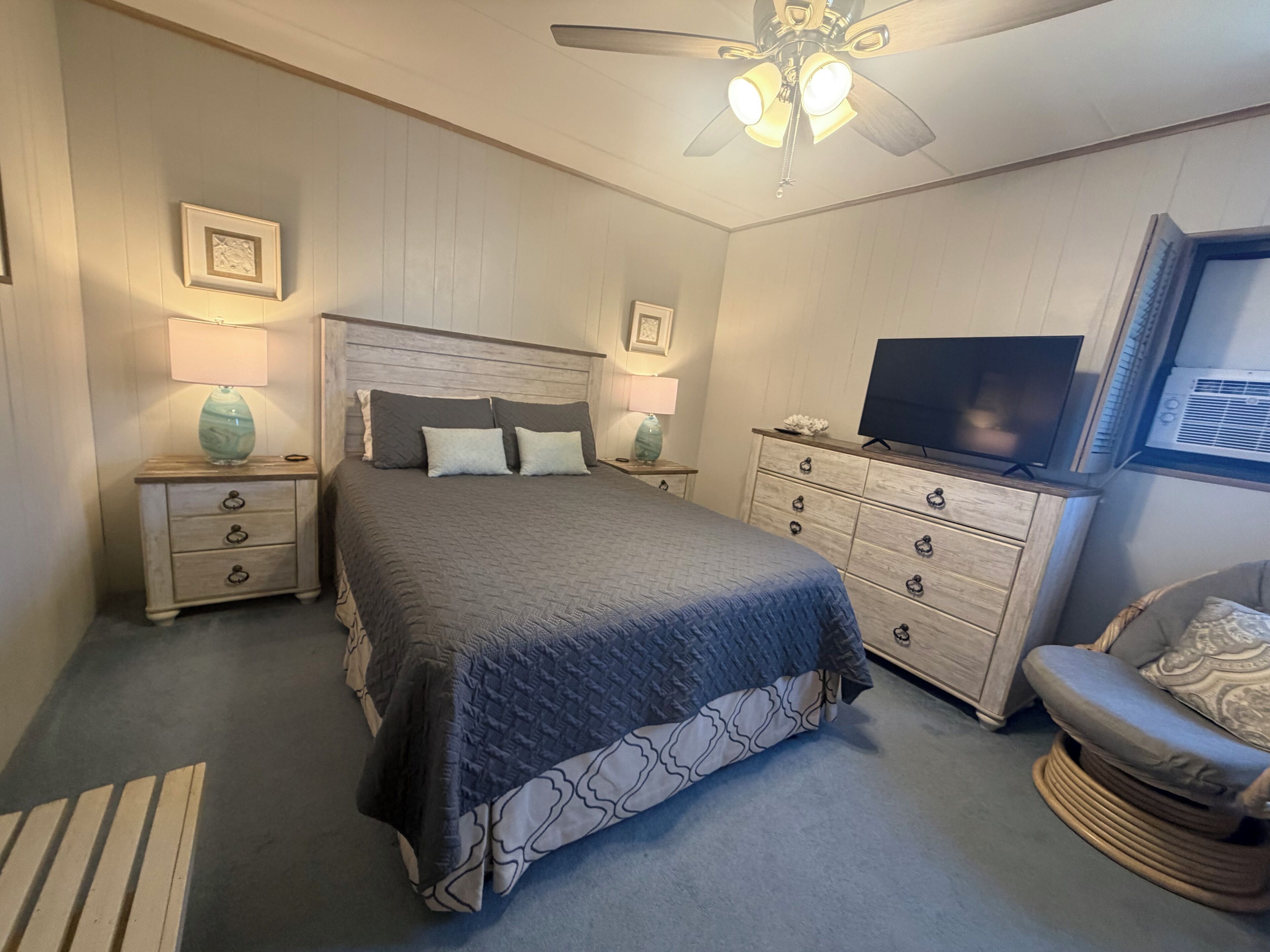 A bedroom with a bed, nightstands, a dresser, a television, and a ceiling fan.