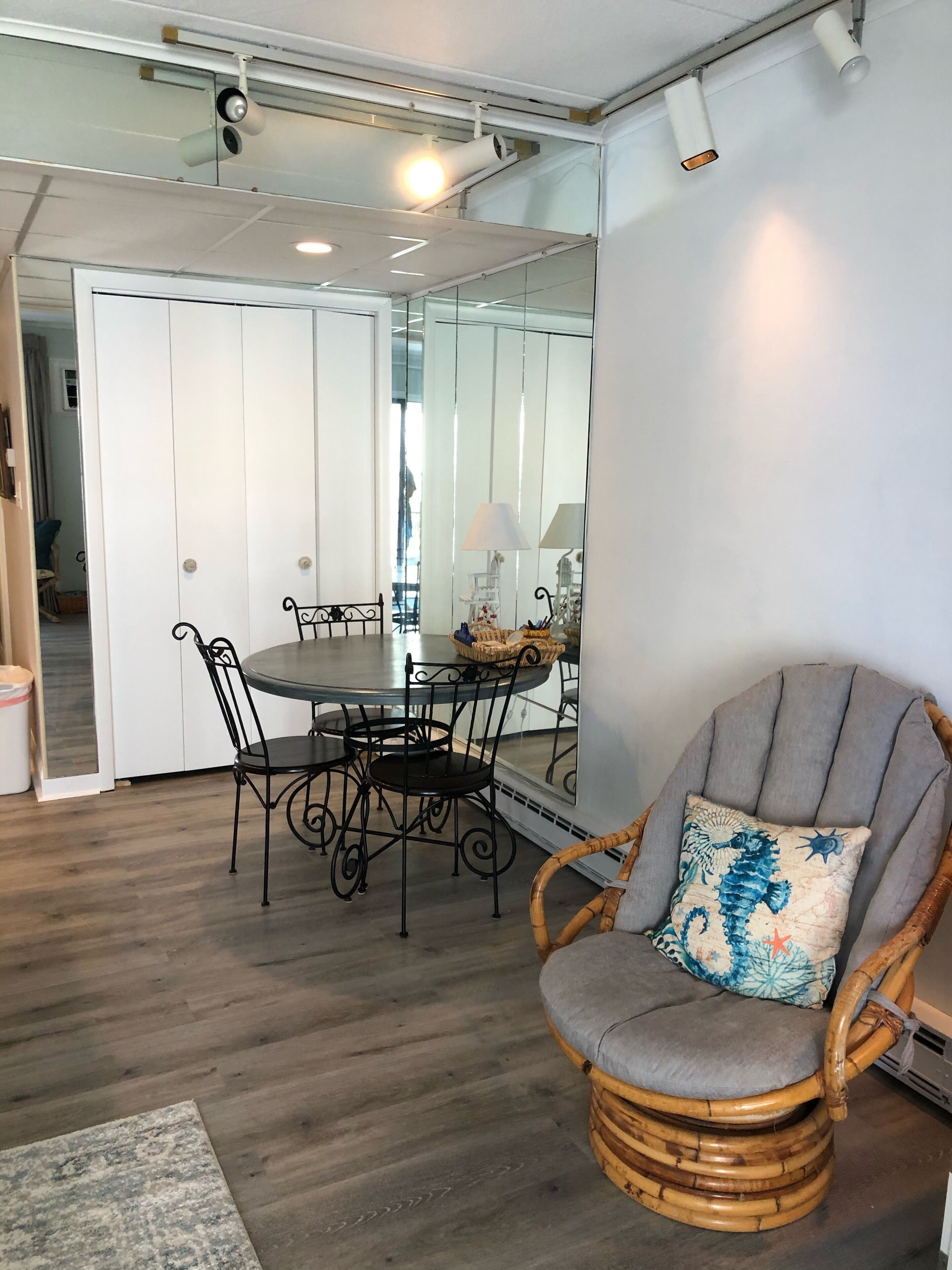 Un coin repas avec une table ronde, des chaises en métal noir et un fauteuil en osier avec un coussin.