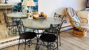 Un comedor con una mesa redonda, sillas negras, una silla de mimbre y un espejo grande que refleja la habitación.