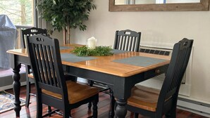 A dining room with a wooden table, four chairs, a potted plant, and a mirror on the wall.