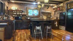Une cuisine avec un îlot central en bois, des tabourets de bar, un réfrigérateur et une fenêtre donnant sur un beau paysage.