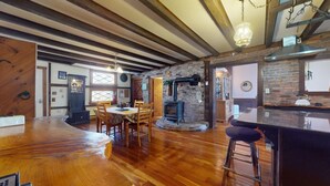 Un intérieur rustique avec des poutres apparentes, une cheminée en pierre, un coin bar en bois et une table à manger avec des chaises.