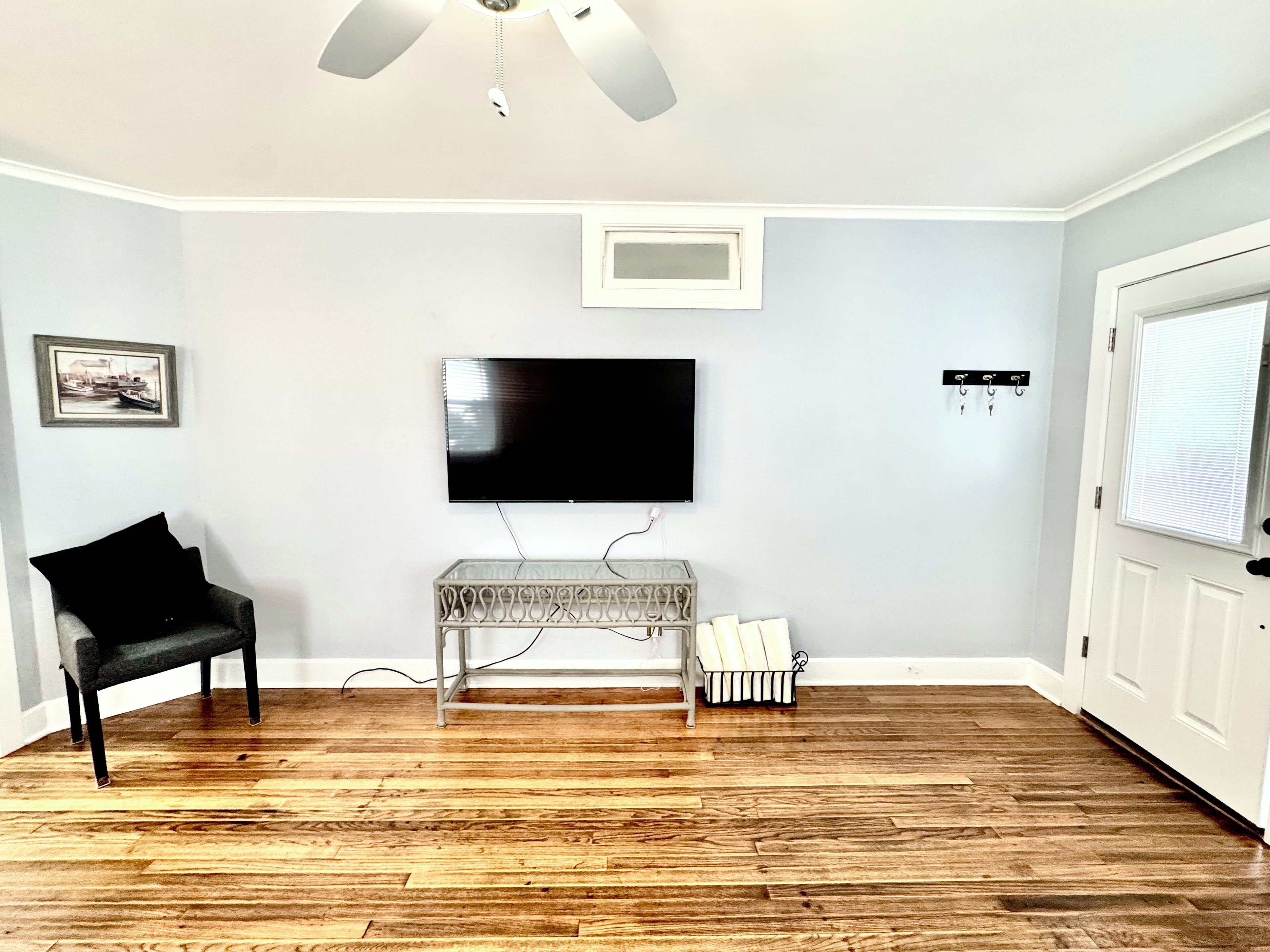 A room with a wooden floor, a black chair, a white bench, a flat-screen TV mounted on the wall, and a door with a window.