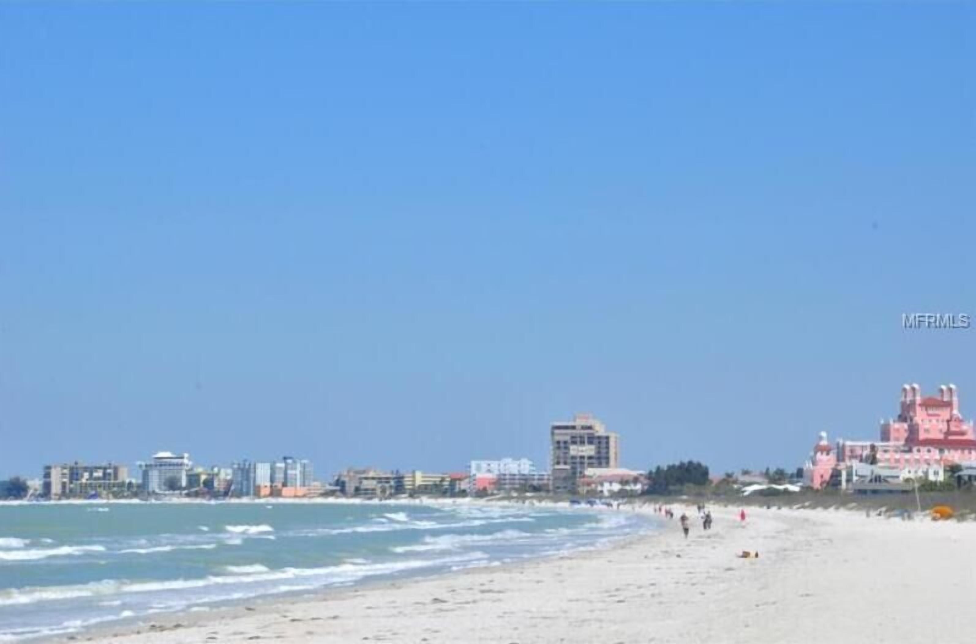 A beach with buildings in the background, including a pink castle-like structure.