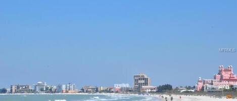 A beach with buildings in the background, including a pink castle-like structure.