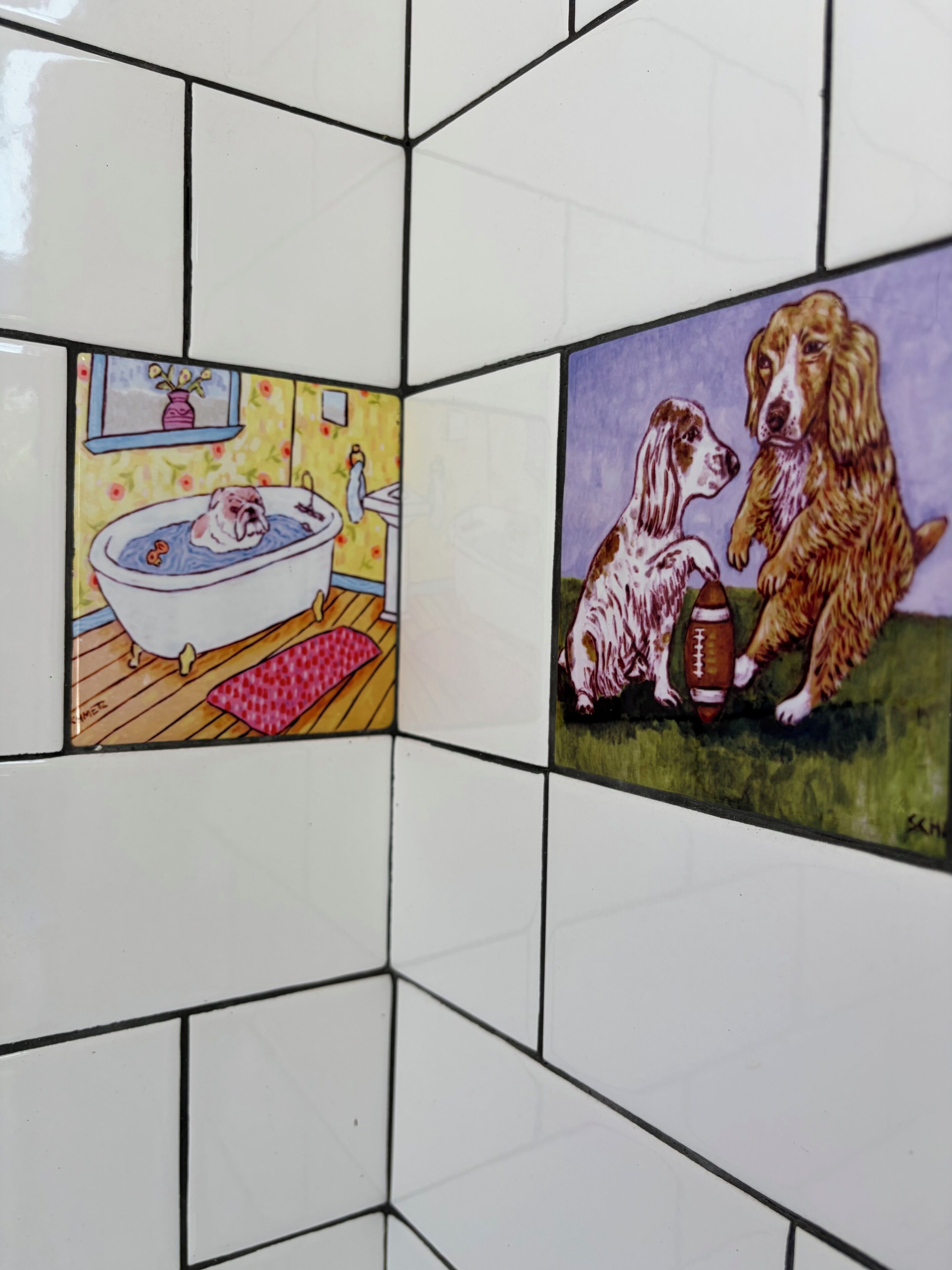 Une salle de bain avec des carreaux blancs et deux carreaux décoratifs représentant des chiens.
