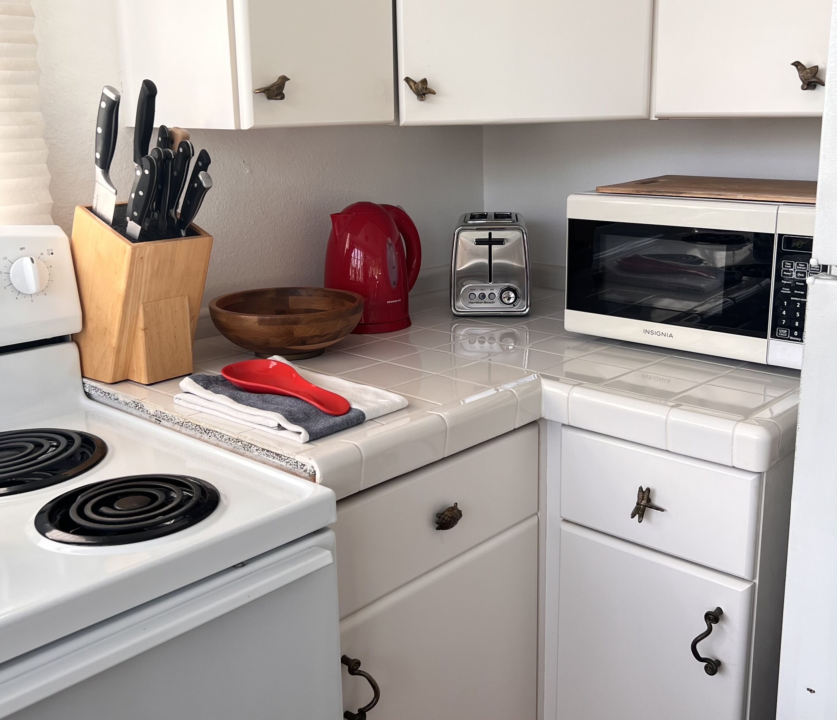 Una cocina con estufa, microondas, tostadora, un cuenco de madera y una tetera roja.