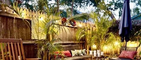 Un espace extérieur accueillant, aménagé avec un banc en bois, un canapé confortable et un jardinier orné de fleurs rouges.