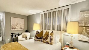 Une chambre à coucher avec un grand lit, une chaise, une table de chevet et une lampe.