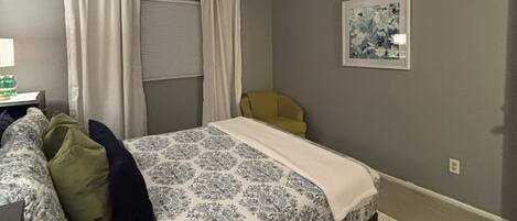 Une chambre à coucher avec un lit, un ventilateur de plafond, une chaise, une lampe et un tableau au mur.