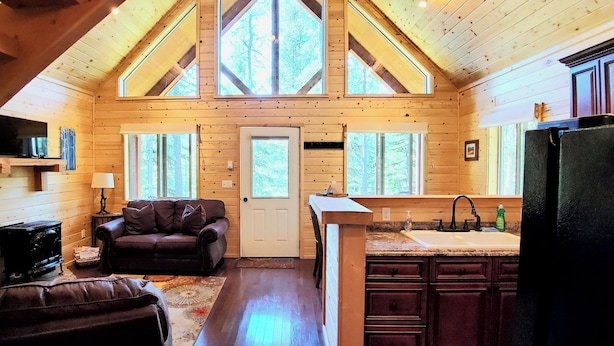 A cabin interior with a loft bedroom, a living area with a sofa and television, and a kitchen with wooden cabinets and a sink.